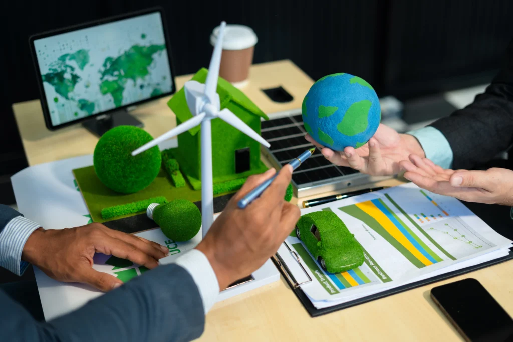 Un grupo de personas analiza gráficos junto a maquetas del planeta y turbinas, mostrando cómo se integra qué es un sistema de gestión ambiental en el análisis estratégico.