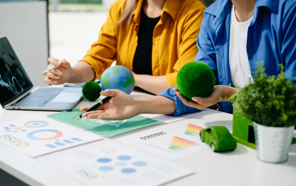 Un grupo de personas analiza documentos y gráficos relacionados con sostenibilidad, mientras manipulan objetos verdes que evocan la naturaleza, en el contexto de la elaboración de Reportes ESG.
