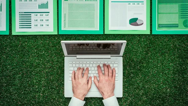 Una persona redacta un reporte de sustentabilidad mientras revisa gráficos y datos que reflejan el desempeño ambiental y social de la empresa.