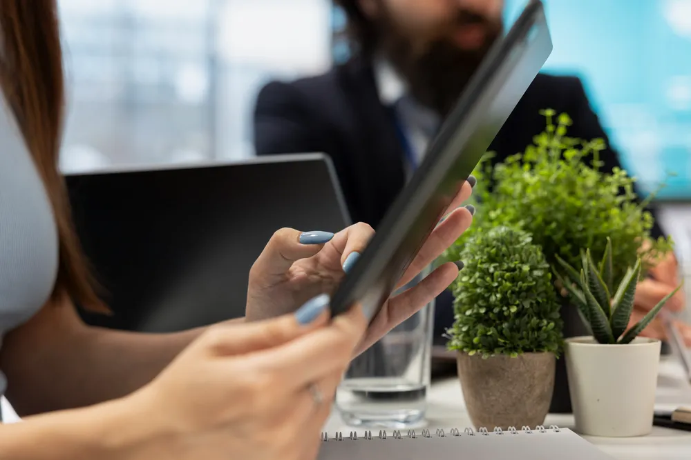 Una persona utiliza una tablet junto a una planta sobre la mesa, simbolizando la conexión entre tecnología, sostenibilidad y valor compartido.