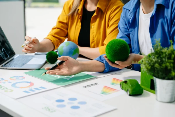 Dos personas revisan informes ambientales y estrategias verdes utilizando objetos simbólicos del planeta, reflejando cómo Workiva apoya la elaboración de reportes sostenibles.